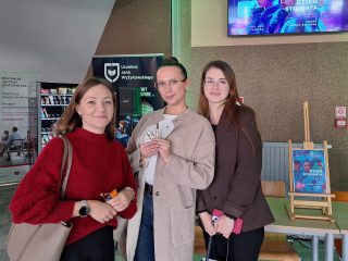 Trzy uczestniczki Dnia Studenta pozują przy stoliku ze słodyczami.