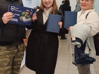 Trzy osoby pozują z materiałami UJW na korytarzu podczas Dnia Studenta.