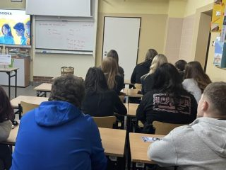 Uczniowie przy ławkach oglądają slajd prezentowany podczas wizyty UJW.