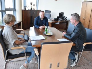 Troje uczestników spotkania omawia dokumenty dotyczące transportu przy biurowym stole.