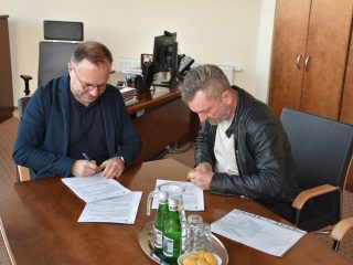 Dwaj mężczyźni podpisują dokumenty dotyczące transportu dla studentów UJW.