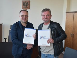 Dwaj mężczyźni prezentują teczki z logo UJW i podają sobie dłonie.