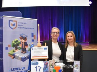 Dwie przedstawicielki UJW pozują za stoiskiem targowym z materiałami promocyjnymi.
