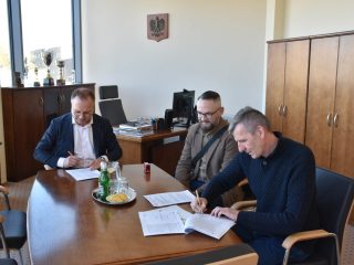 Podpisywanie dokumentów dotyczących transportu w obecności trzech uczestników spotkania.