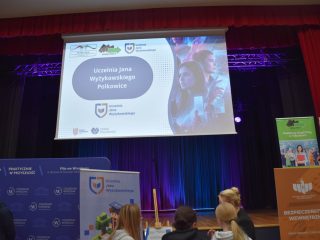 Ekran nad sceną targową wyświetla prezentację Uczelni Jana Wyżykowskiego w Polkowicach.