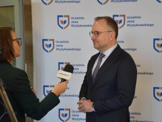 Mężczyzna udziela wywiadu dziennikarce z mikrofonem na tle logo UJW.