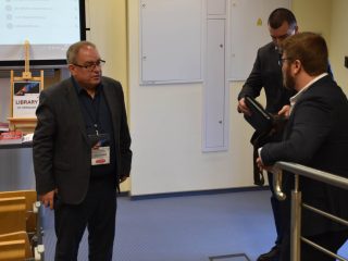 Uczestnicy konferencji rozmawiają przy balustradzie obok ekspozycji książek.