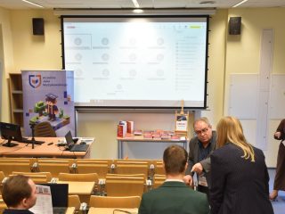 Widok sali konferencyjnej z połączeniem online na ekranie i ekspozycją książek.