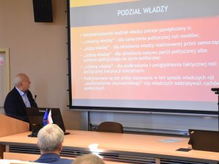 Prelegent omawia slajd „Podział władzy” w sali konferencyjnej.