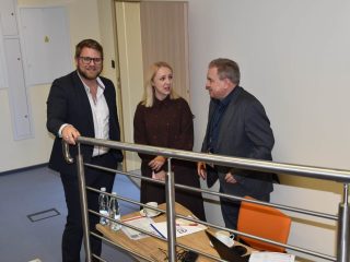 Troje uczestników konferencji rozmawia przy balustradzie w sali wykładowej.