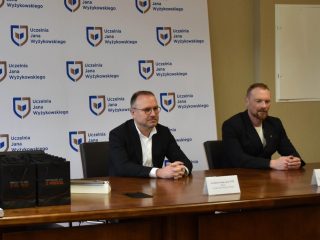 Dwaj przedstawiciele siedzą przy stole z torbami upominkowymi podczas wręczenia certyfikatów KGHM.
