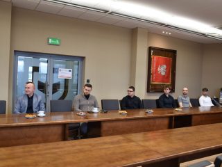 Uczestnicy uroczystości KGHM siedzą w rzędzie przy długim stole.