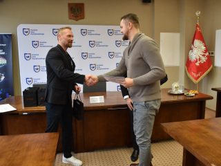 Uczestnik w szarym swetrze odbiera gratulacje uściskiem dłoni.