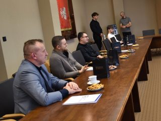 Uczestnicy z certyfikatami i torbami upominkowymi rozmawiają przy stole.