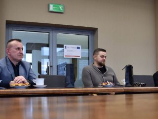 Uczestnicy uroczystości wręczenia certyfikatów KGHM siedzą przy stole z poczęstunkiem.