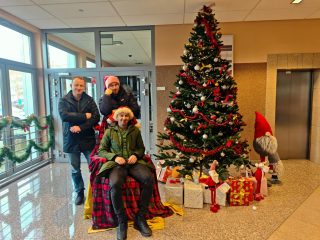 Trzech uczestników mikołajek pozuje przy fotelu i świątecznych prezentach.