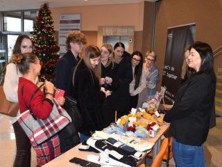 Grupa uczestników przy stoisku pracodawcy z kolorowymi gadżetami i materiałami.