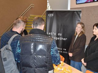 Uczestnicy spotkania przy banerze CCC słuchają informacji o firmie.