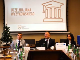 Troje przedstawicieli UJW siedzi pod ekranem z nazwą uczelni.