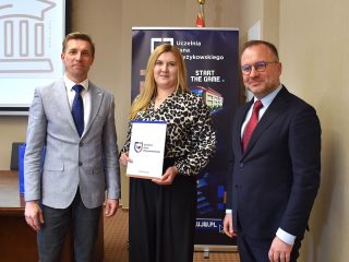 Kobieta we wzorzystej bluzce prezentuje dokument na wspólnym zdjęciu z przedstawicielami UJW.