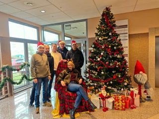 Grupa uczestników mikołajek pozuje z kobietą siedzącą na świątecznym fotelu.