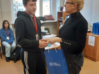 Prowadząca wręcza uczniowi niebieską torbę upominkową.