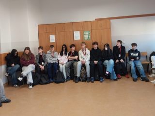 Uczestnicy warsztatów siedzą w kręgu wzdłuż ścian sali.
