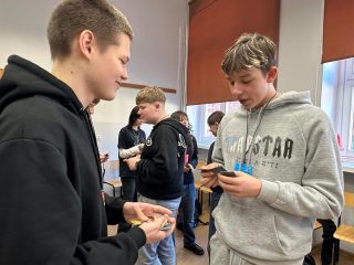 Dwaj uczniowie porównują karty i rozmawiają podczas gry handlowej.