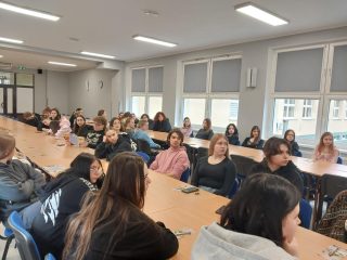 Uczniowie siedzą przy stołach podczas spotkania z przedstawicielem UJW.