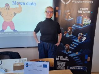 Prowadząca przy ekranie ze slajdem o mowie ciała i banerze UJW.