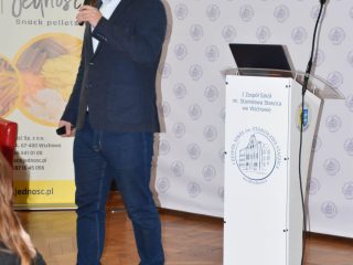 Prelegent przemawia do mikrofonu obok mównicy podczas Dnia Logistyka we Wschowie.