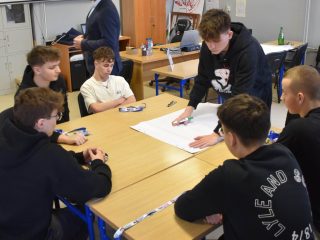 Uczeń pochyla się nad arkuszem grupy podczas warsztatów z okazji Dnia Logistyka.