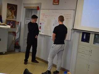 Dwaj uczniowie prezentują pracę zespołu przy tablicy z arkuszami.