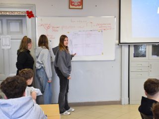Trzy uczennice przedstawiają pracę zespołu przed tablicą podczas warsztatów.