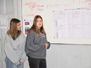 Dwie uczennice omawiają arkusz pracy zespołu przy tablicy podczas Dnia Logistyka.