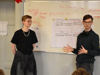 Dwaj uczniowie prezentują pomysły zapisane na arkuszu; jeden gestykuluje.