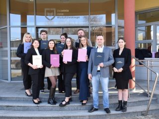 Absolwenci z oprawionymi pracami dyplomowymi pozują na schodach przed wejściem do UJW.