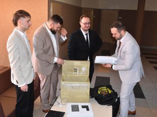 Czterej mężczyźni oglądają model urządzenia ustawiony na stoliku na korytarzu UJW.