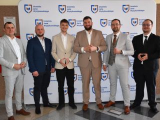 Sześciu absolwentów pozuje w garniturach na tle logo UJW podczas obron inżynierskich.