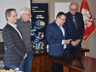 Członkowie komisji podczas odczytywania dokumentu w sali z flagą Polski i banerem UJW.