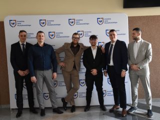 Absolwenci kierunków inżynierskich pozują swobodnie razem przy ściance UJW.