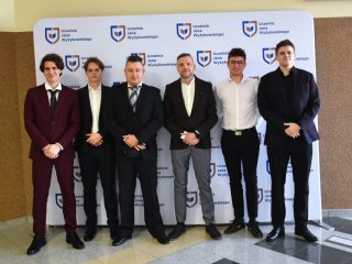 Sześciu uczestników obron inżynierskich pozuje przed ścianką z logo UJW.