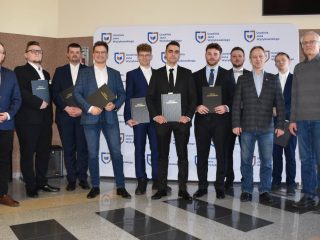 Absolwenci z oprawionymi pracami inżynierskimi na wspólnym zdjęciu z przedstawicielami uczelni.
