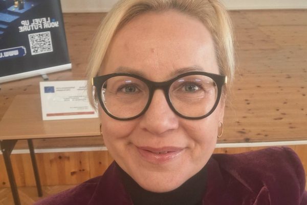 Przedstawicielka UJW w bordowej marynarce pozuje w sali spotkania.