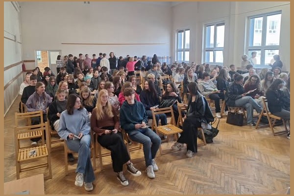 Grupa uczniów siedzi w rzędach krzeseł podczas spotkania z UJW.