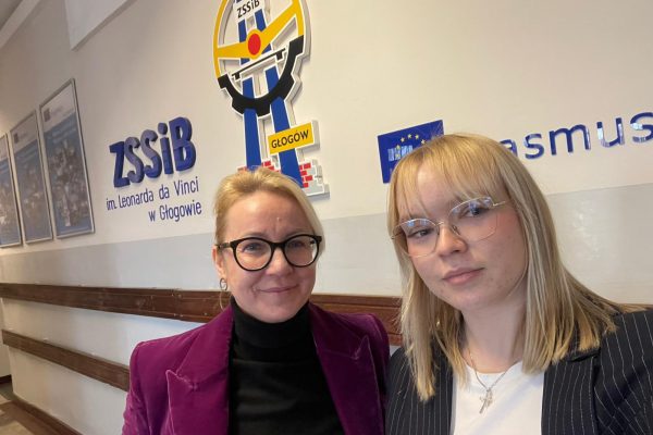 Dwie kobiety pozują przy oznaczeniu Zespołu Szkół Samochodowych i Budowlanych w Głogowie.