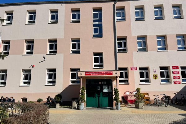 Fasada szkoły z wejściem, tablicami instytucji i stojakiem na rowery.