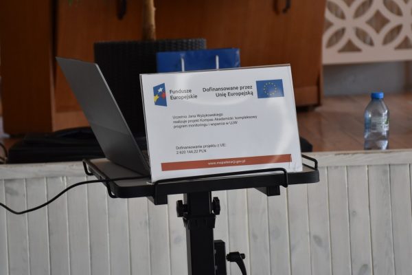 Laptop i tabliczka informująca o dofinansowaniu unijnym na pulpicie prowadzącego.