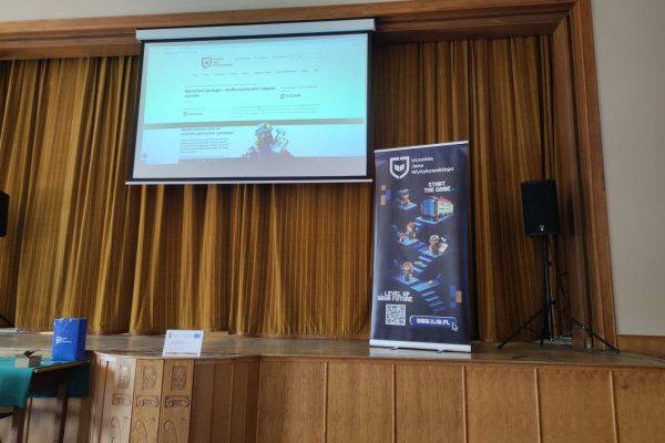 Ekran prezentacji nad sceną z żółtą kurtyną i roll-upem UJW.