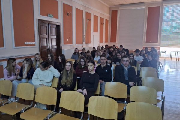 Uczniowie siedzą w rzędach krzeseł w szkolnej auli podczas wizyty UJW.